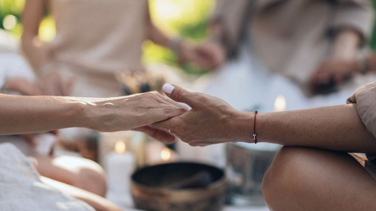 Manos en meditación junto a un cuenco tibetano y velas